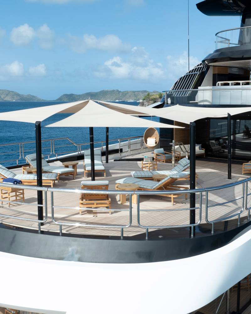 Luxurious loungers and shaded seating areas adorn the deck of this magnificent yacht, set against a backdrop of azure waters and verdant islands.