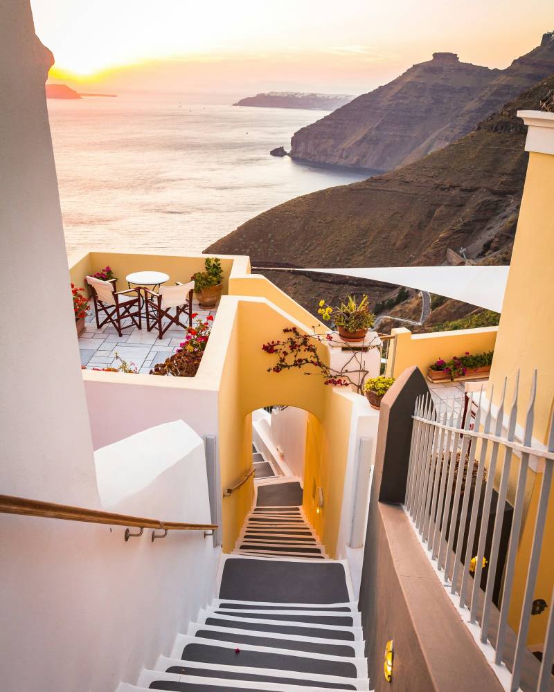 A picturesque Santorini staircase descends towards the Aegean Sea at sunset.