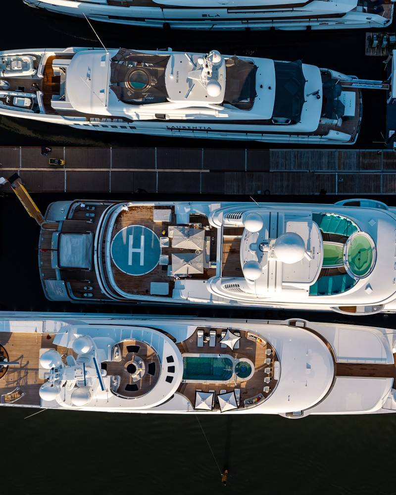 Aerial view of three large yachts docked side-by-side, with a helipad visible on one.