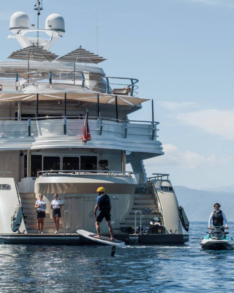 A person on a hydrofoil enjoys the water near a luxurious yacht while two jet skiers follow behind.