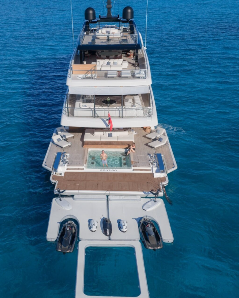 A luxury yacht with a jacuzzi and jet skis floats serenely on the crystal-clear turquoise waters of the Mediterranean.