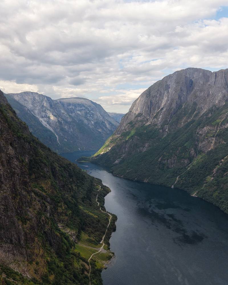 A majestic fjord surrounded by towering, rugged mountains, with a winding river or lake visible in the valley below.