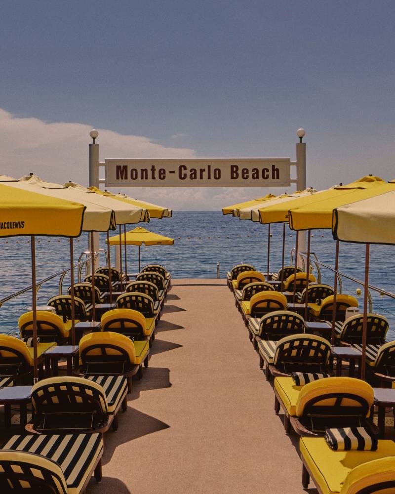 Yellow and cream umbrellas shade empty lounge chairs on a wooden deck beside a tranquil blue sea.