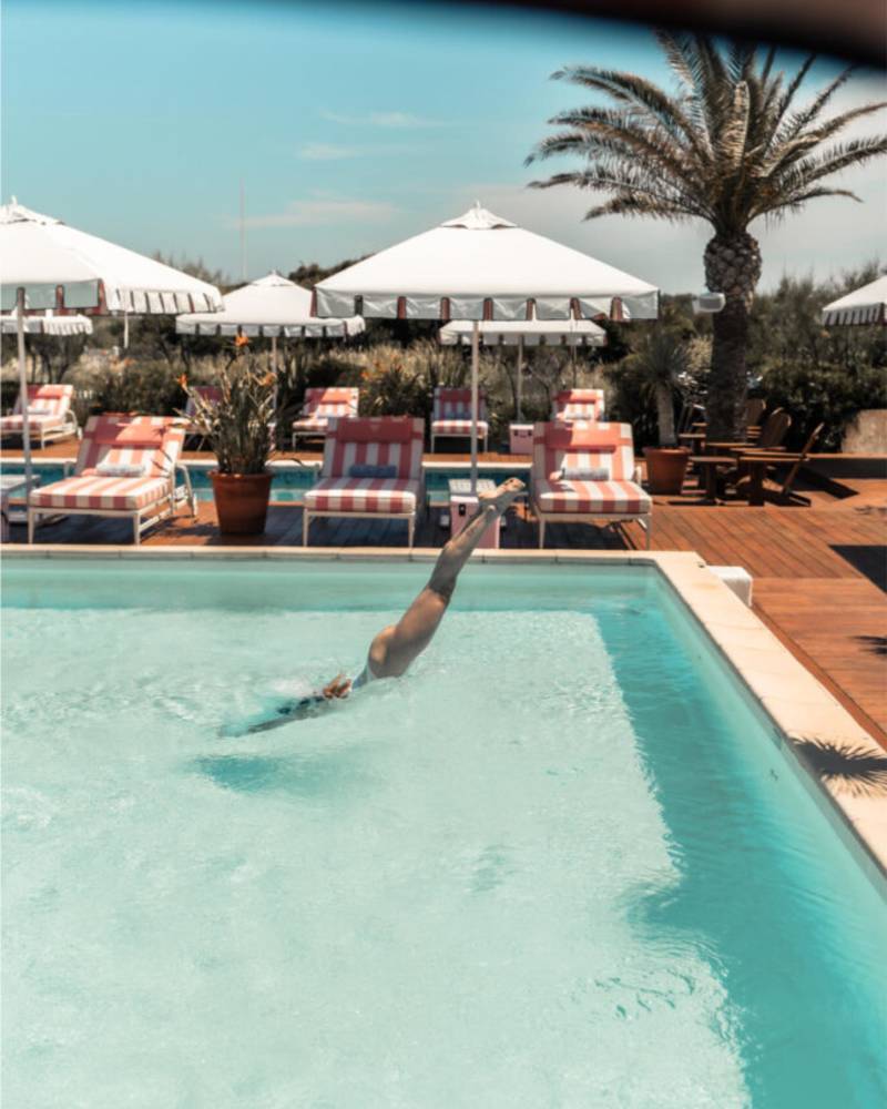 Row of empty lounge chairs with pink and white striped cushions awaits guests under a matching striped awning.