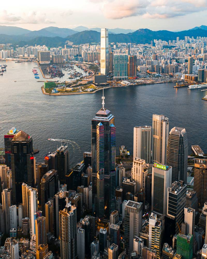 A dense cityscape of skyscrapers rises from the water's edge, with a vast expanse of buildings and mountains stretching into the distance.