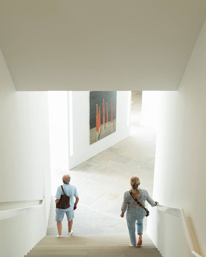 Two people descend a bright, modern staircase towards a contemporary art exhibition in the background.