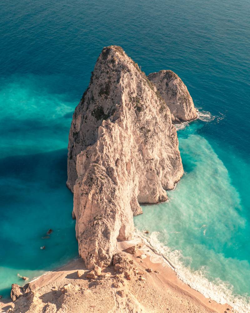 A towering, rocky island juts out from the turquoise waters, with a sandy beach in the foreground.