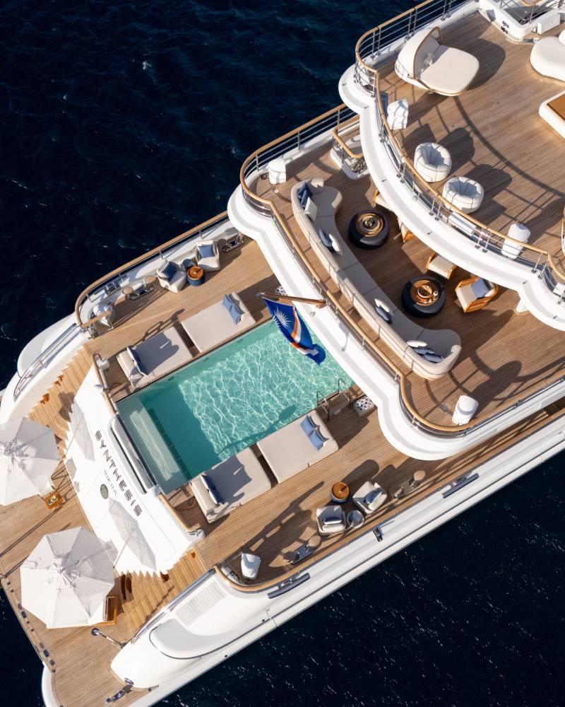 A luxurious yacht with a swimming pool and lounge areas on its deck floats on the deep blue ocean.