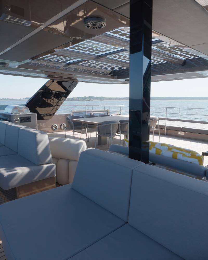 Plush grey seating arrangements fill the foreground of a modern yacht's deck, while the background reveals a calm ocean under a clear sky.