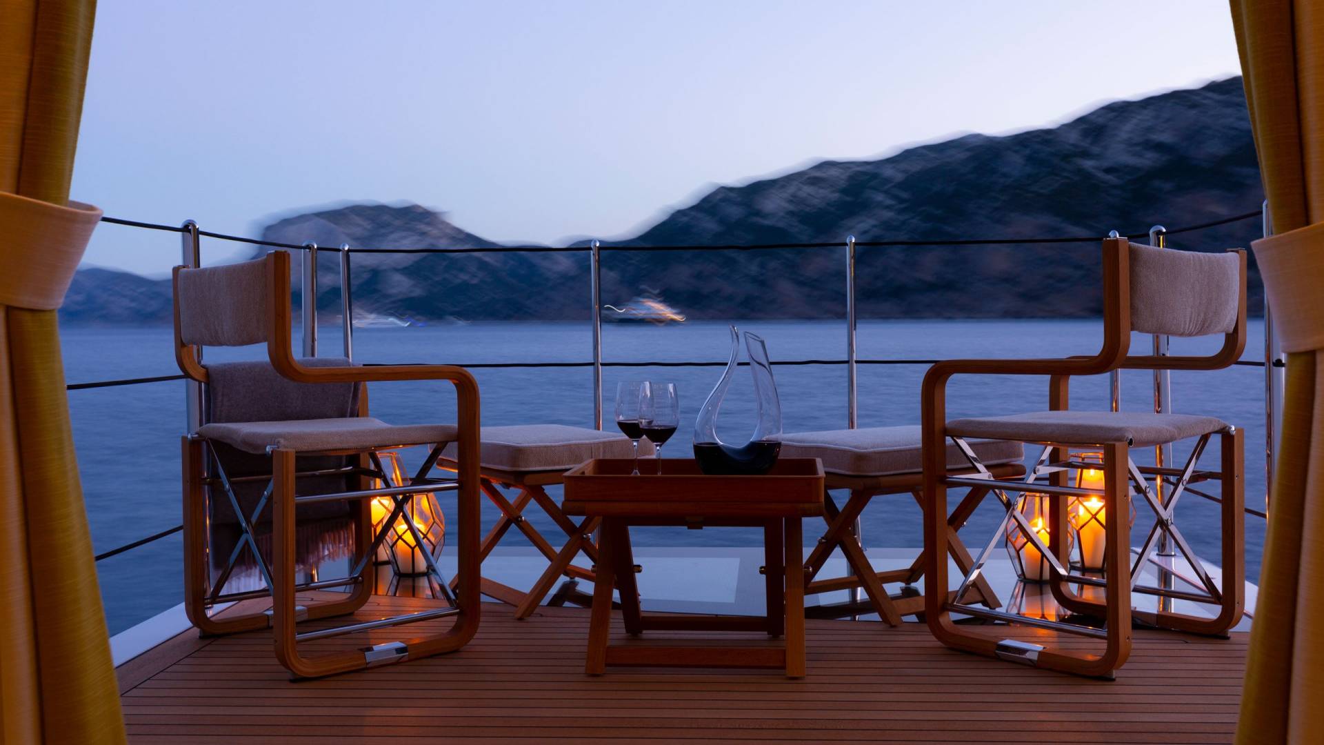Enjoy a serene evening with wine on deck as mountains fade into the twilight.