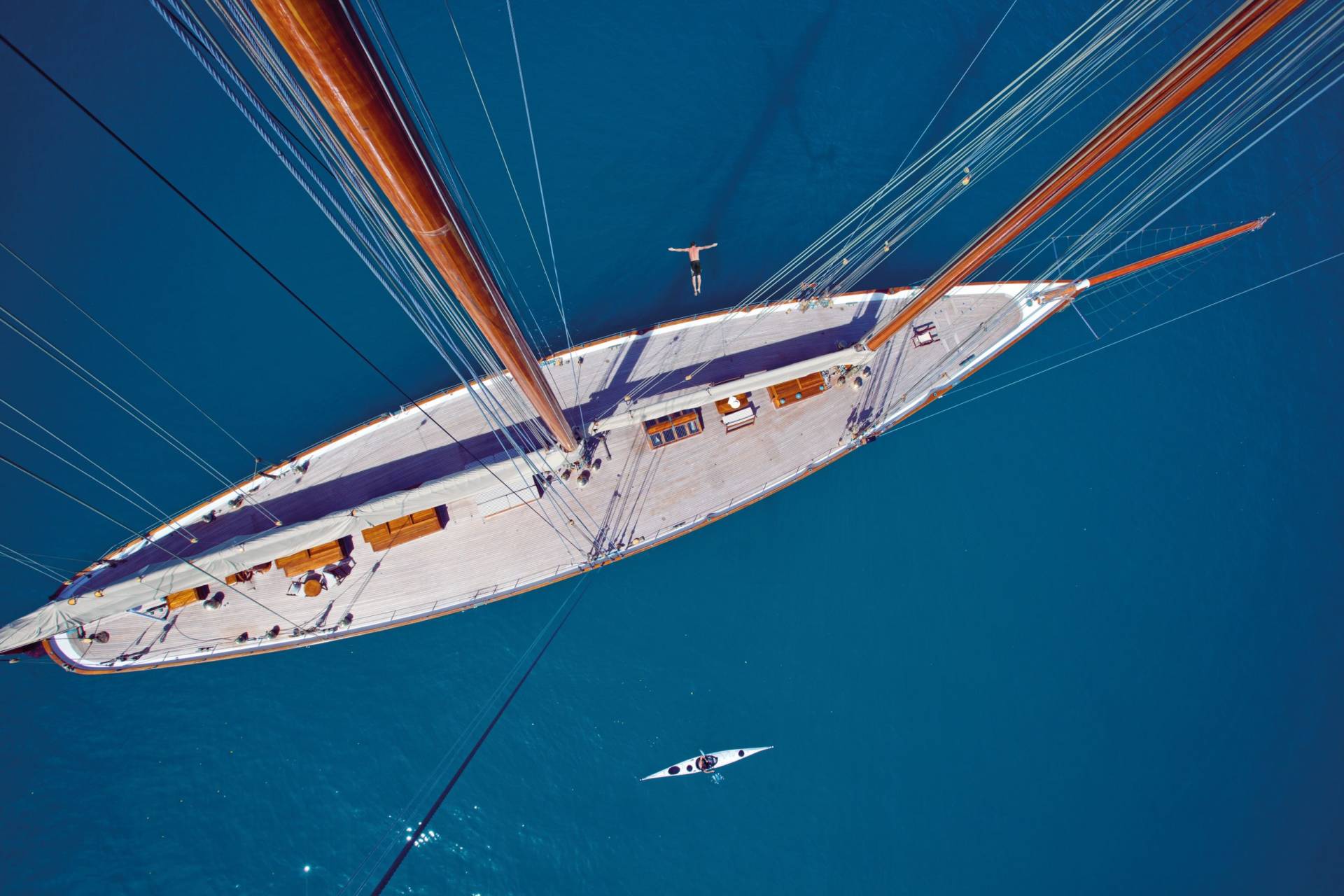 A lone kayaker paddles in the deep blue sea near a majestic wooden sailboat with towering masts.