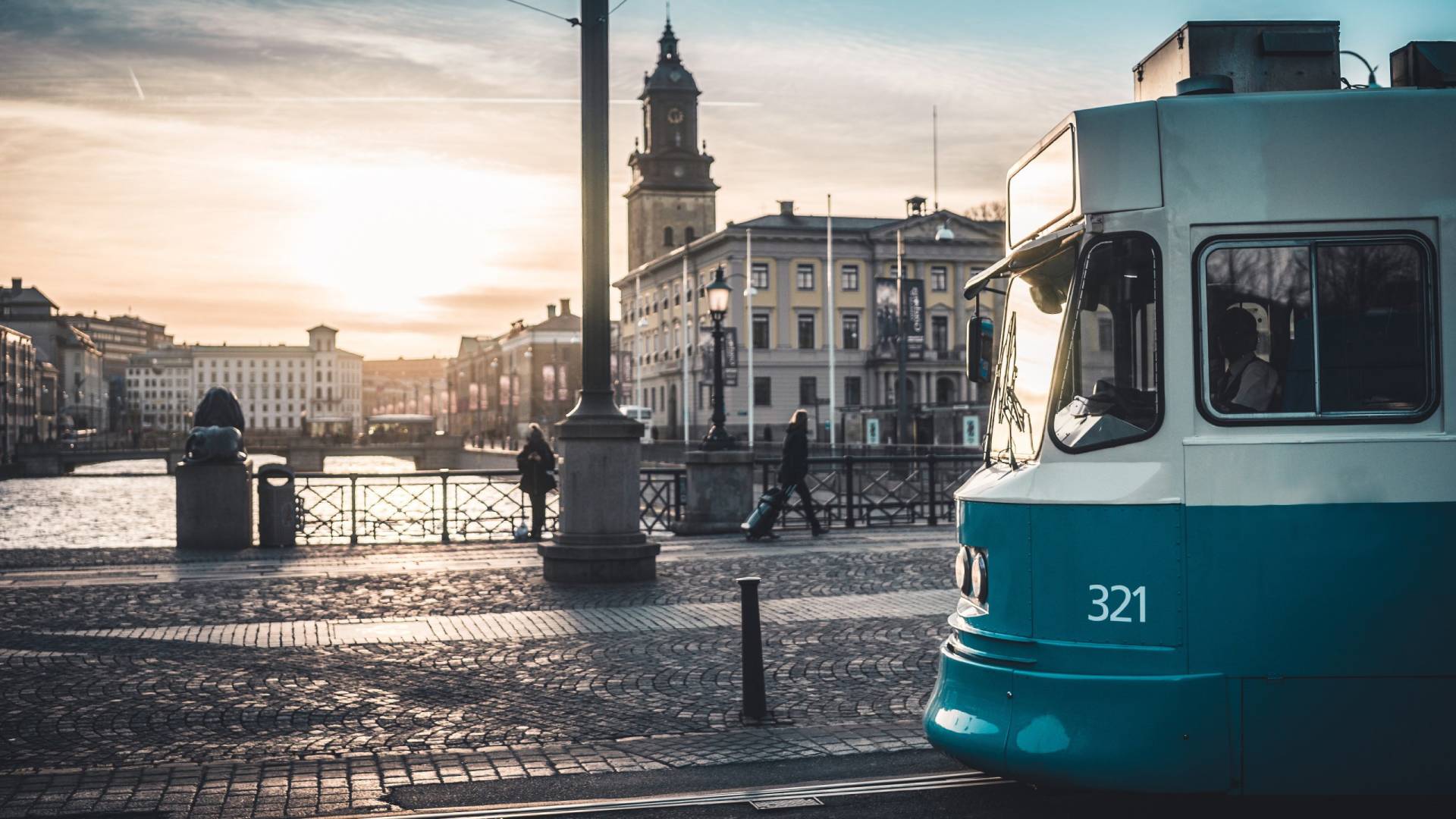 A tram numbered 321 glides along cobblestone tracks beside a canal at sunset in a European city.