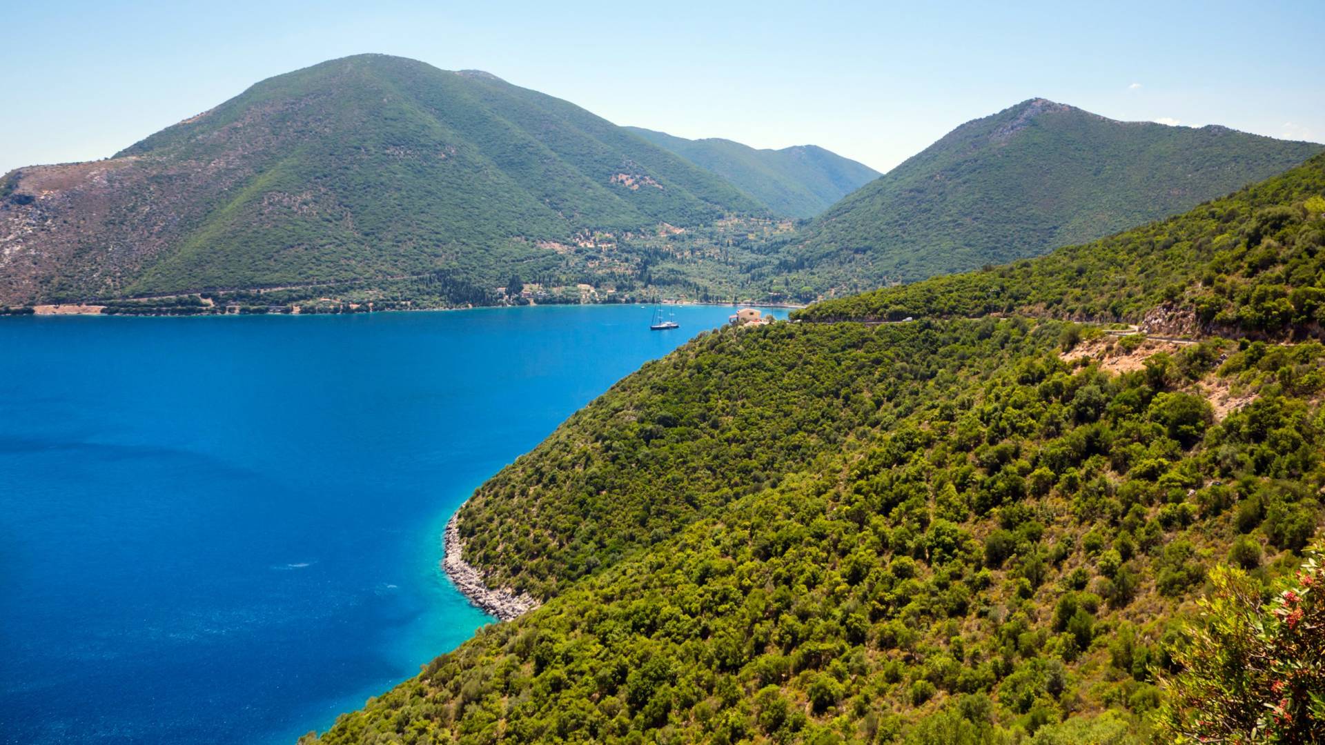 Lush green mountains plunge into the brilliant blue waters of a serene bay.