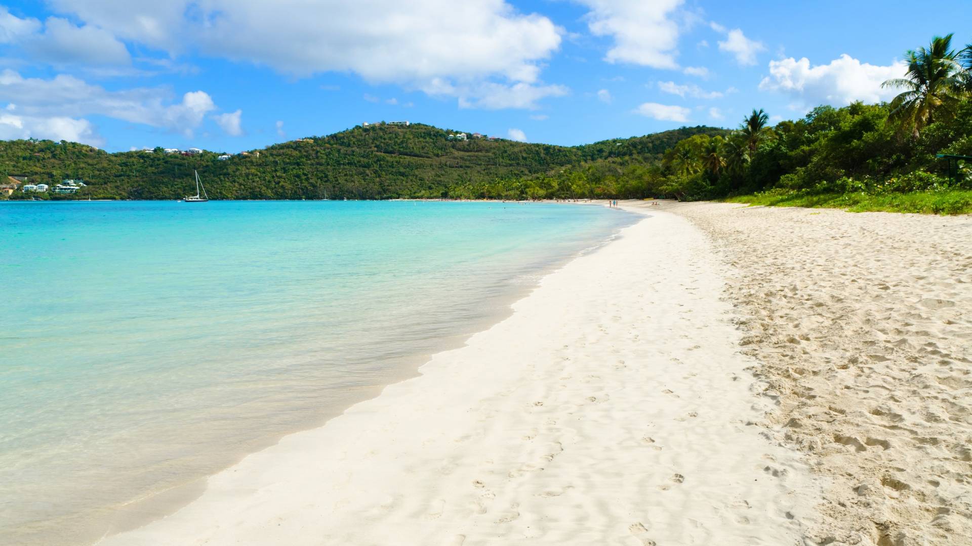 A pristine white sand beach meets the crystal-clear turquoise waters of the Caribbean under a bright blue sky.