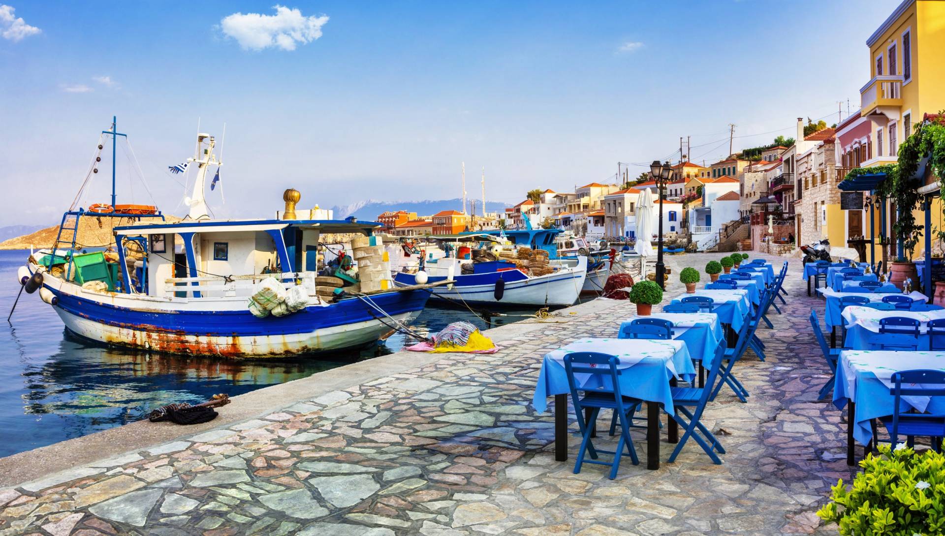 Charming fishing boats are moored in a picturesque harbor lined with tables set for outdoor dining.
