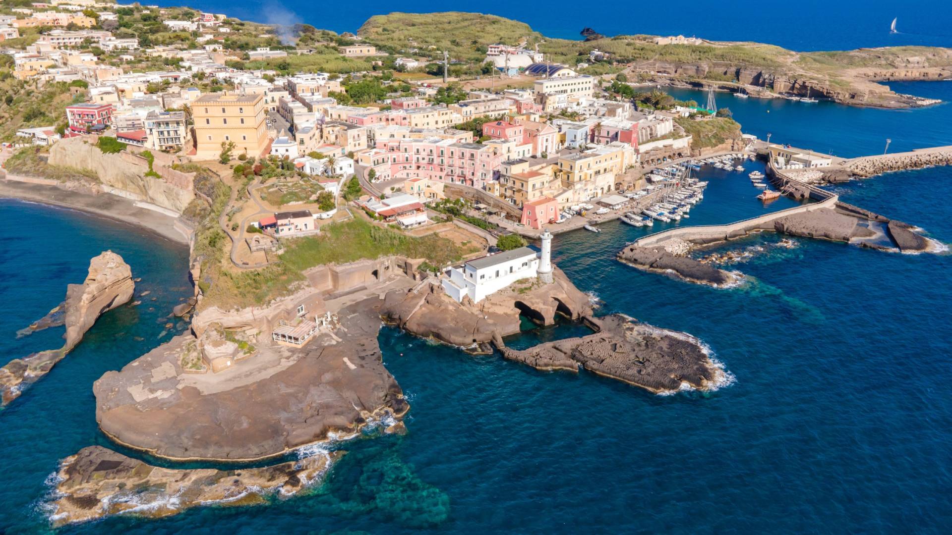A vibrant coastal village with colorful buildings cascades down a hillside to a bustling harbor filled with boats.