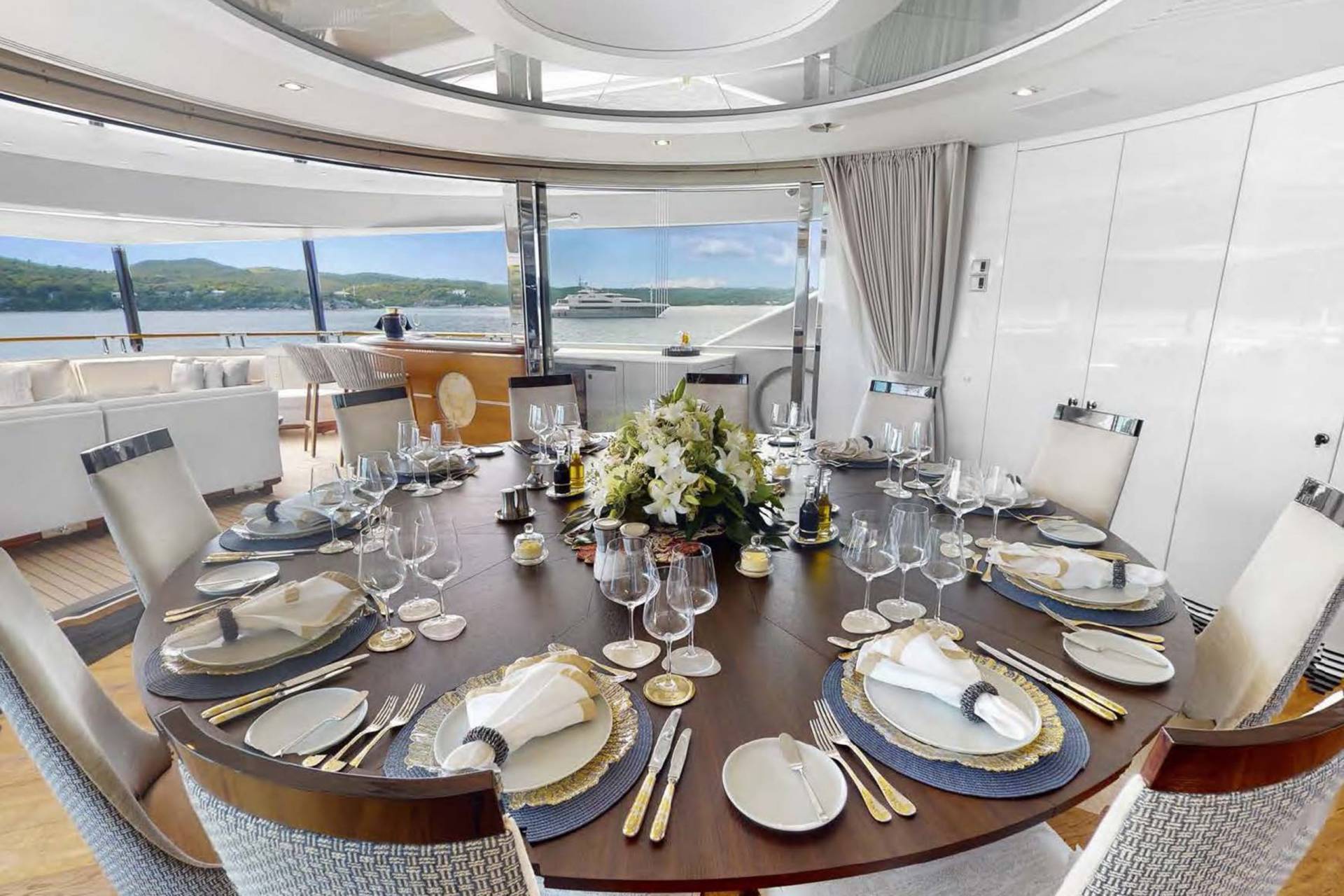 A beautifully set dining table awaits guests on a luxurious yacht with a scenic ocean view.