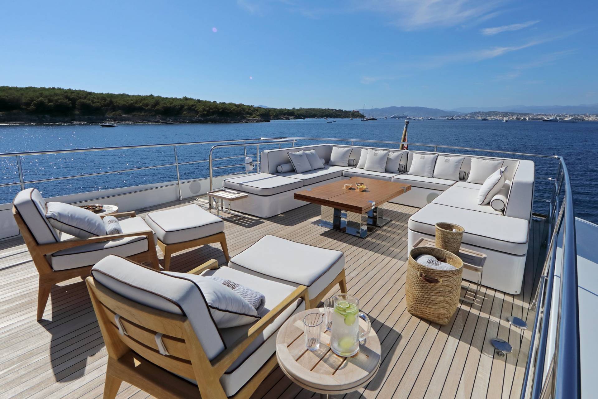 Relax on the spacious deck of a luxury yacht, surrounded by plush seating and the sparkling blue sea.