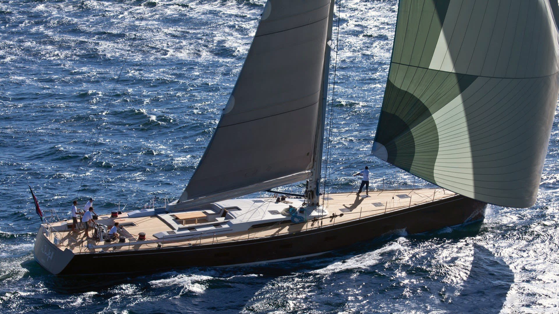 A sleek yacht cuts through the sparkling blue ocean, its sails billowing in the wind.