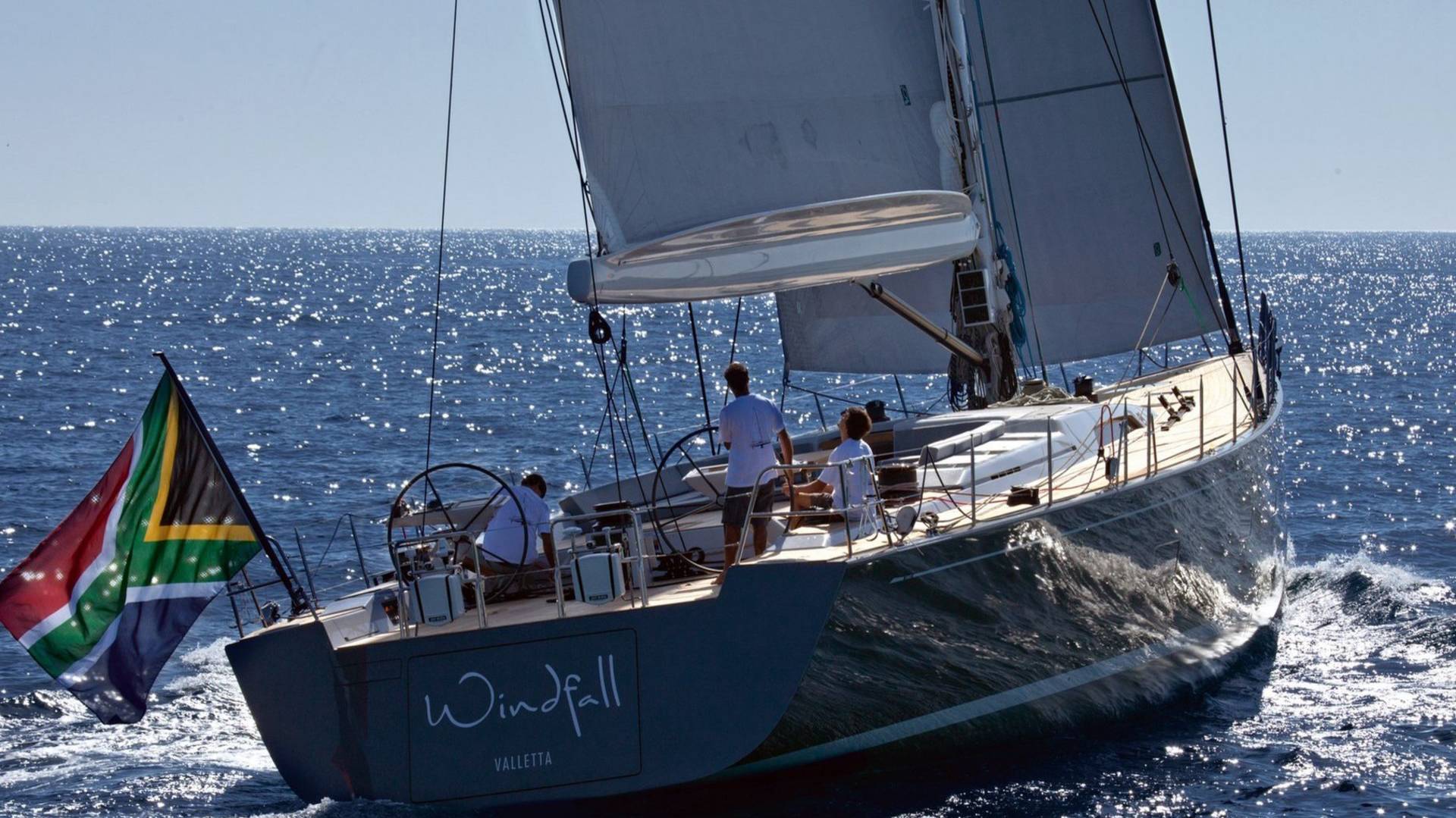 A sleek sailboat with the South African flag proudly displayed cuts through the sparkling blue ocean waters.