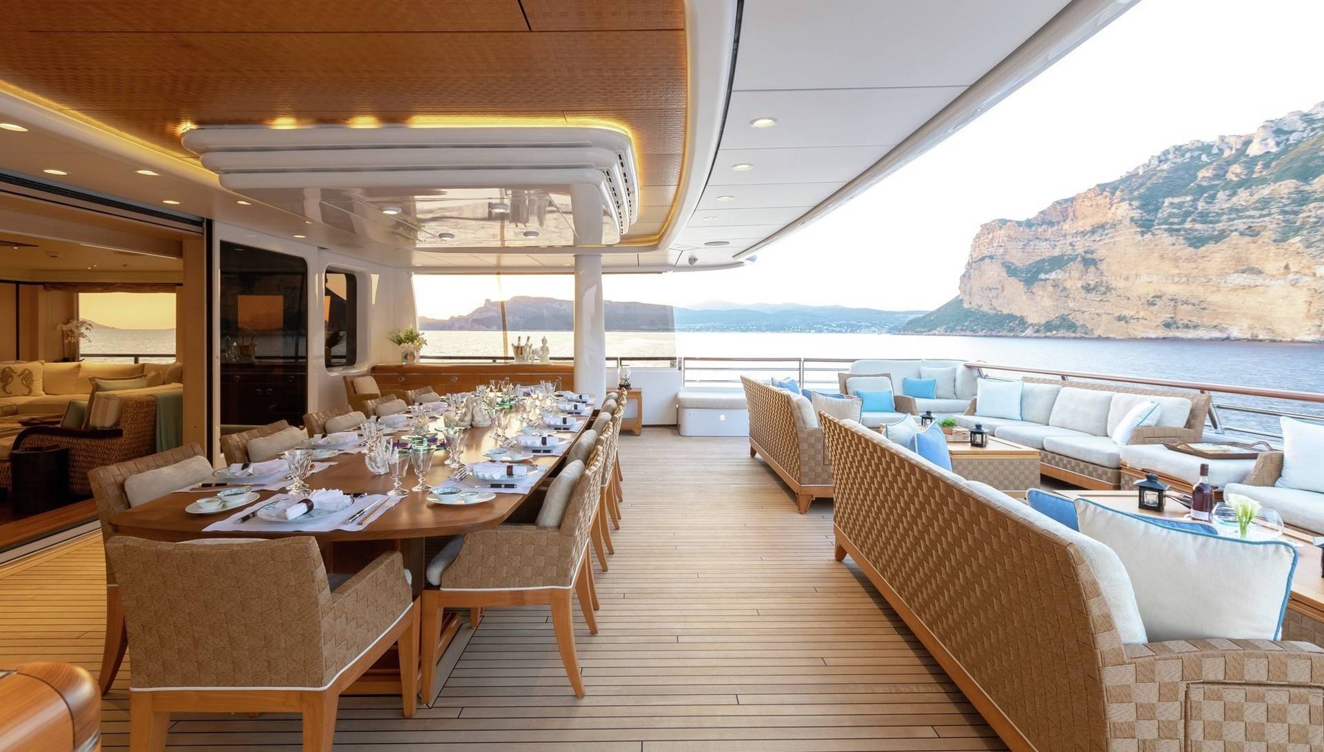 Dine al fresco on a lavish yacht deck overlooking a dramatic coastal landscape at sunset.