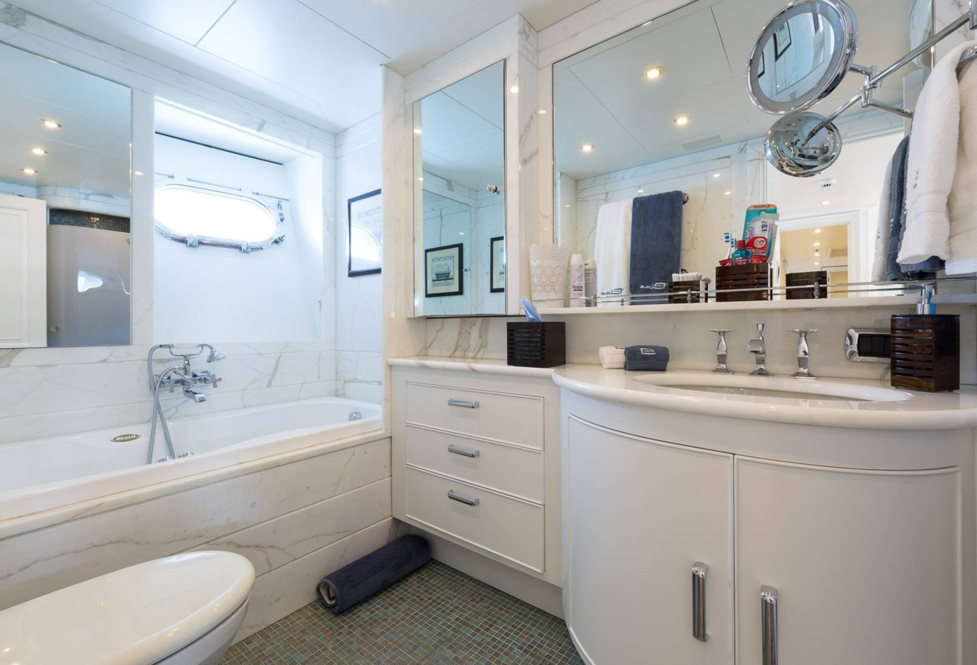 Luxurious marble finishes and a porthole window create a serene spa-like atmosphere in this elegant yacht bathroom.