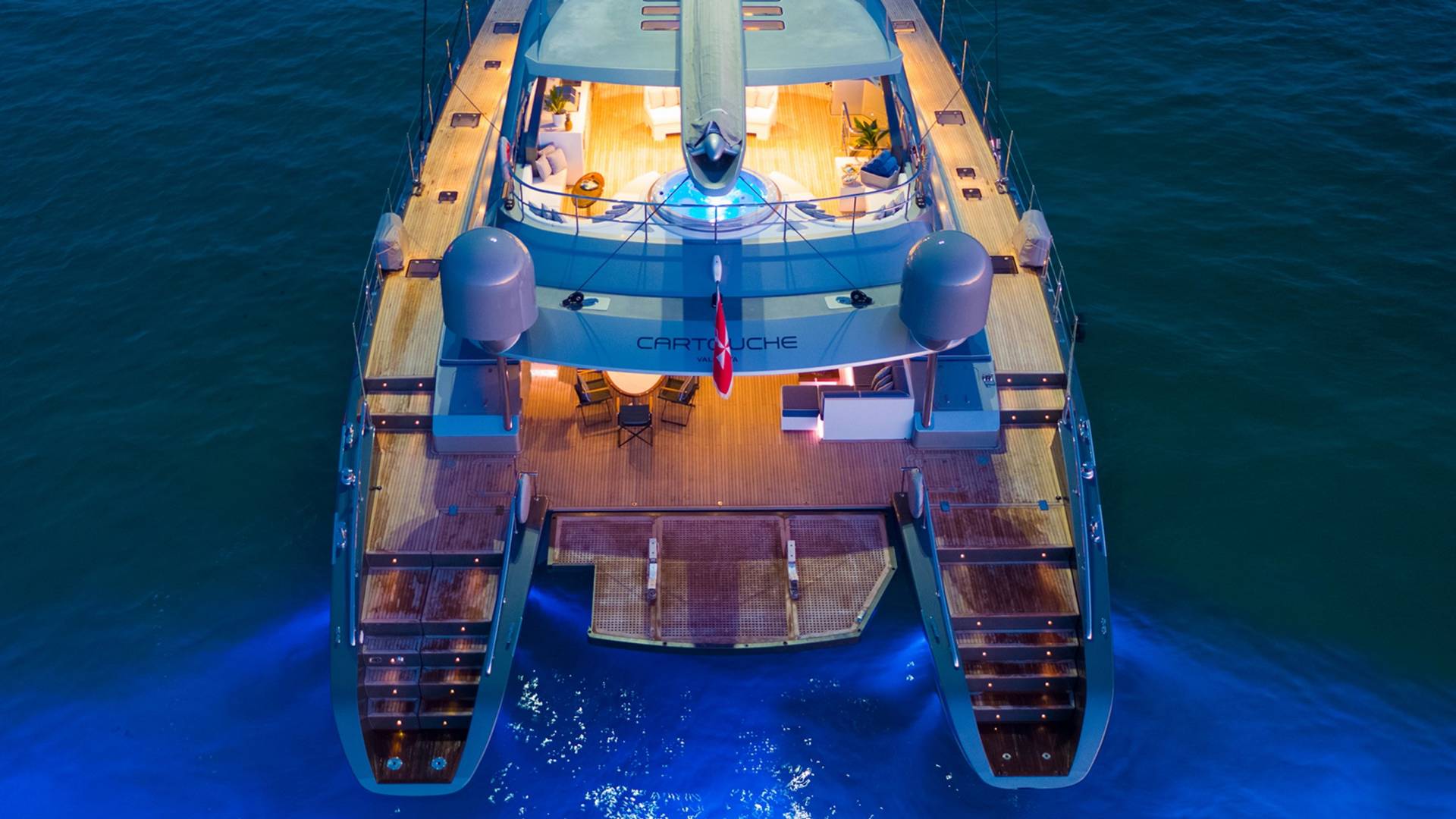 A luxurious catamaran yacht glows with blue underwater lights as it rests on calm, dark waters.