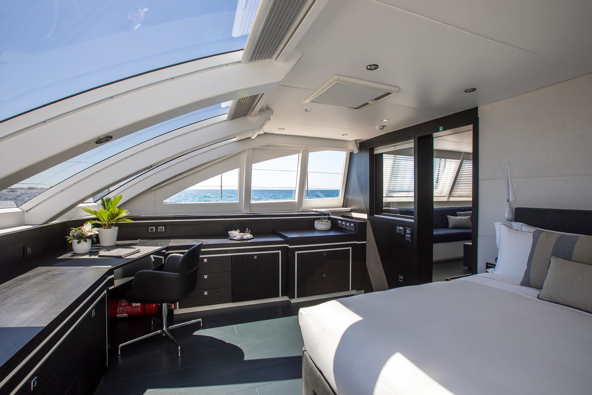 A modern yacht cabin offers a luxurious workspace with ocean views and a comfortable bed.