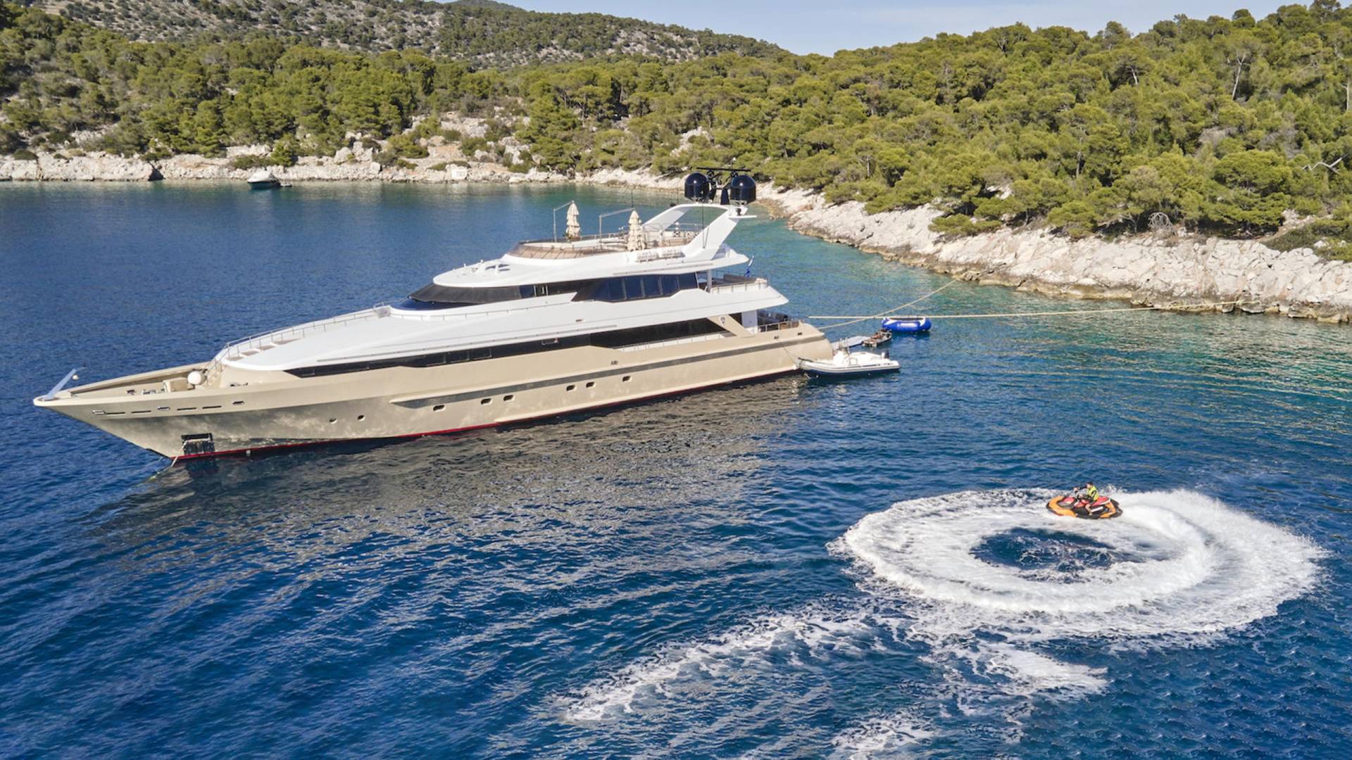 A luxurious yacht anchors in a secluded cove while guests enjoy a thrilling ride on a jet ski.
