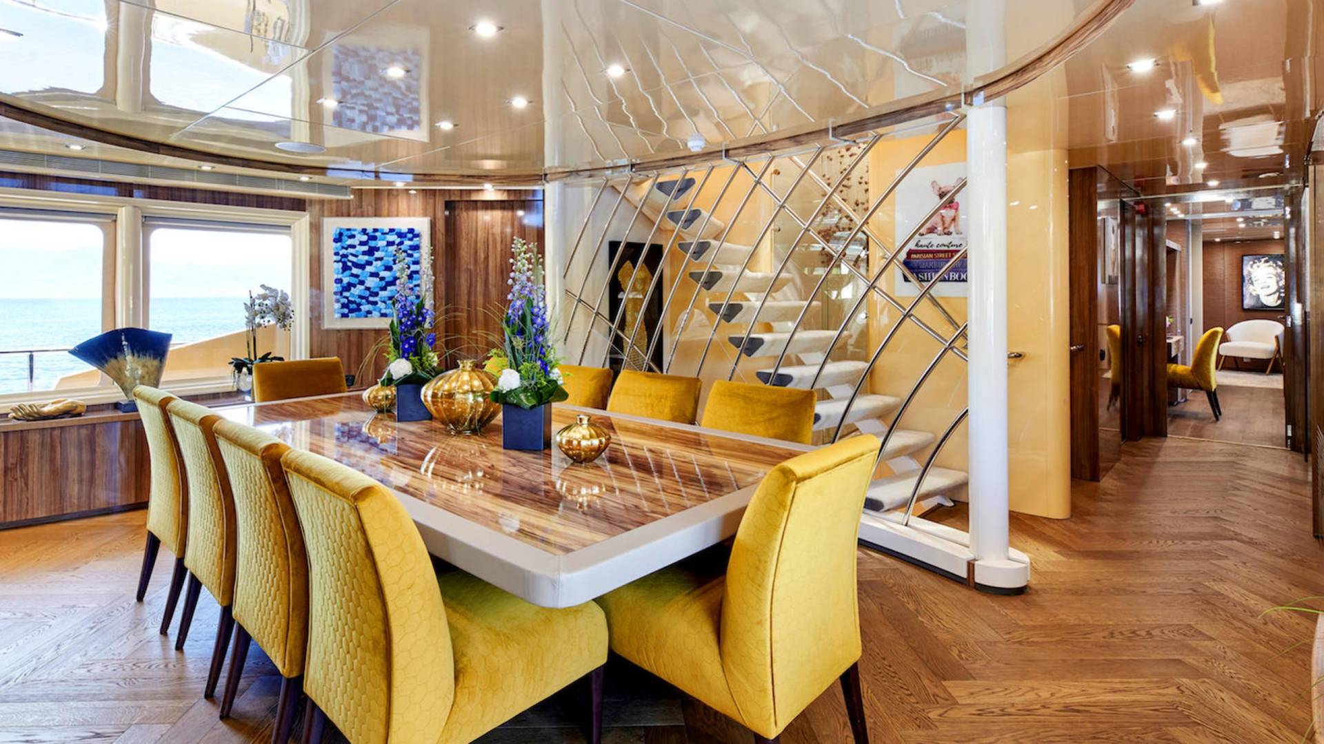 Luxurious yellow chairs surround a polished dining table set with golden vases and floral arrangements on a yacht.