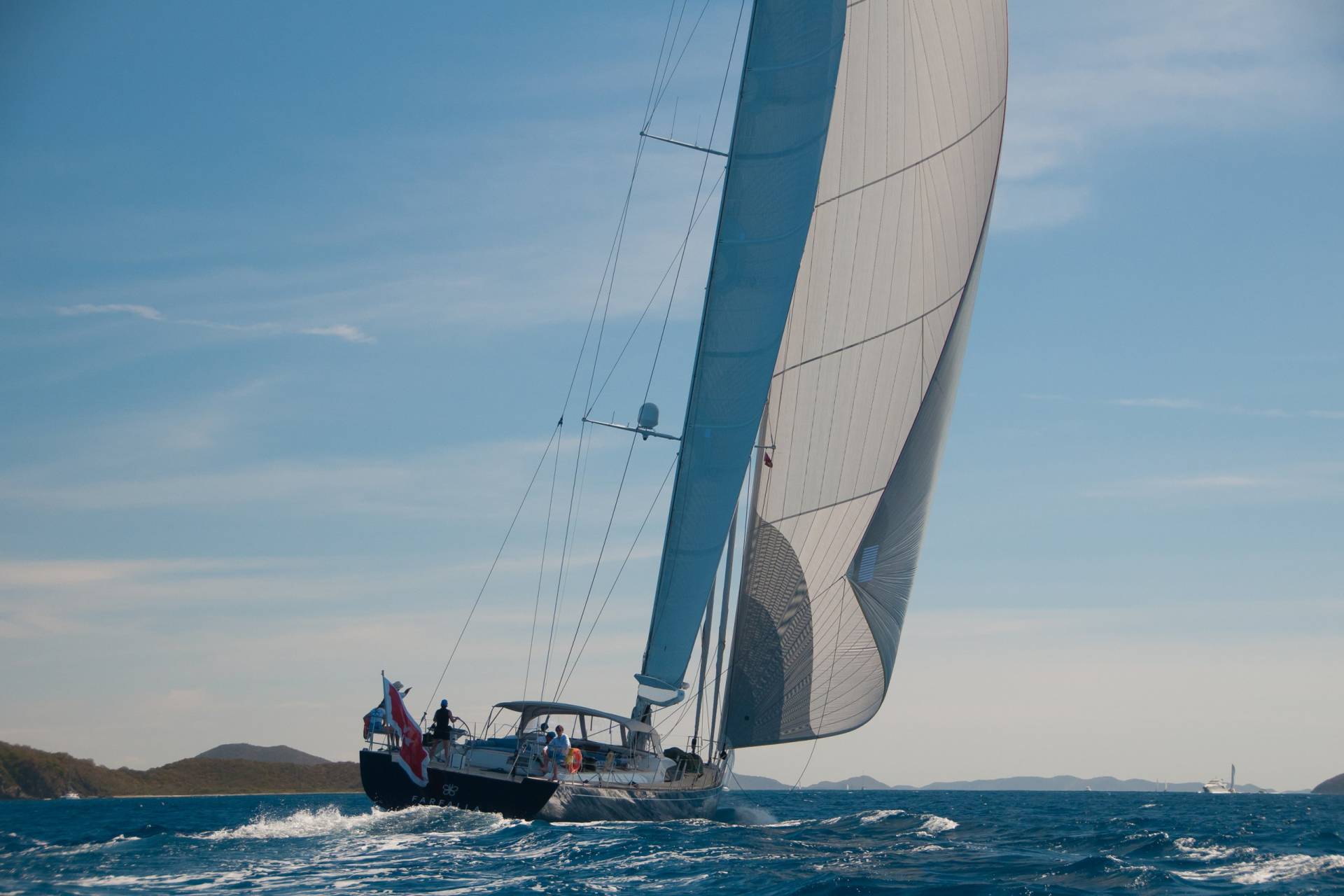 A majestic sailboat glides through the azure waters under a clear blue sky, its sails billowing in the gentle breeze.