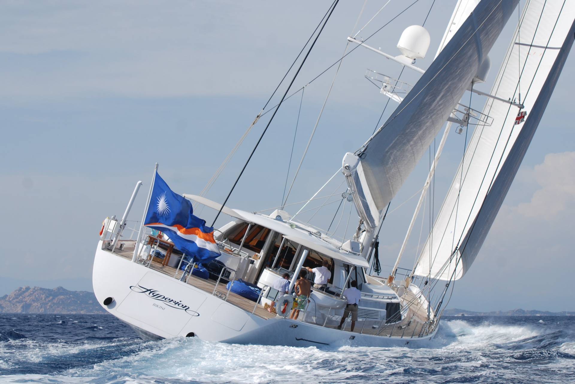 A majestic sailing yacht cuts through the choppy blue sea under a bright sky with its sails full.