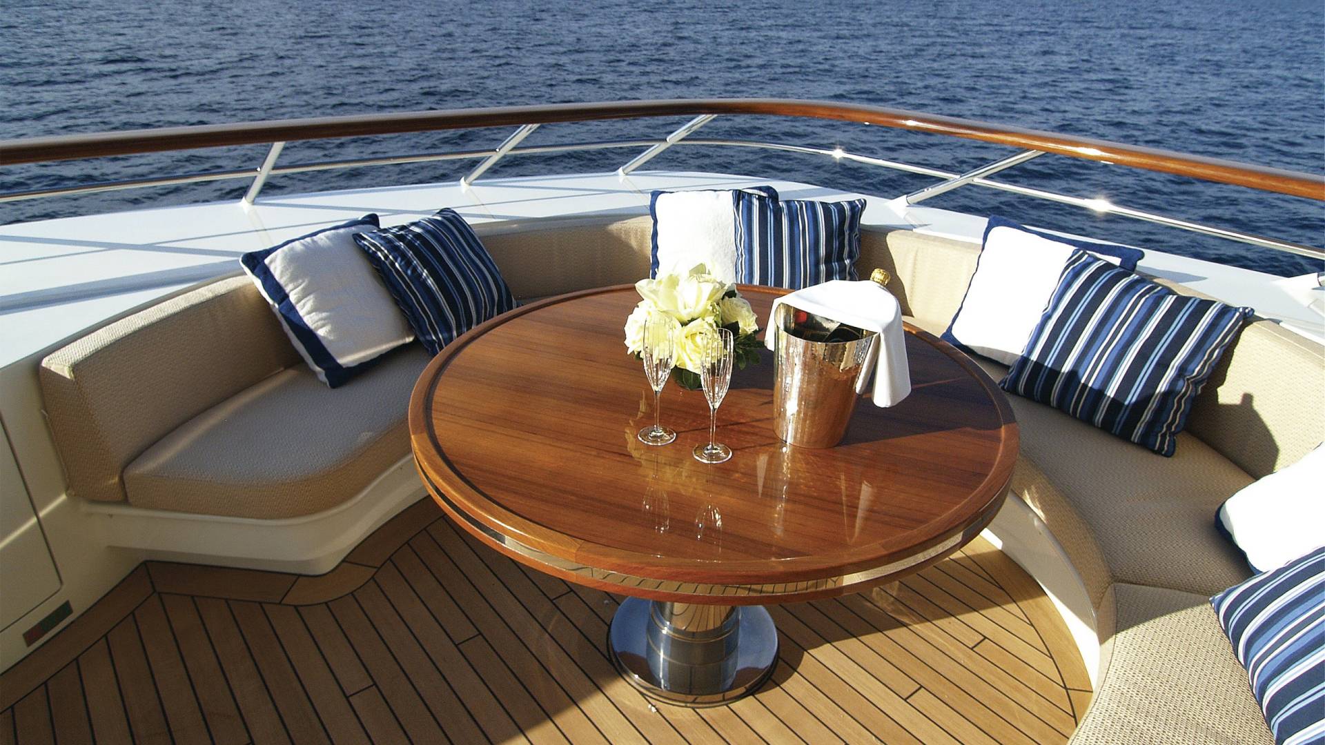 Champagne awaits on the deck of a luxurious yacht, surrounded by plush seating and the sparkling blue sea.