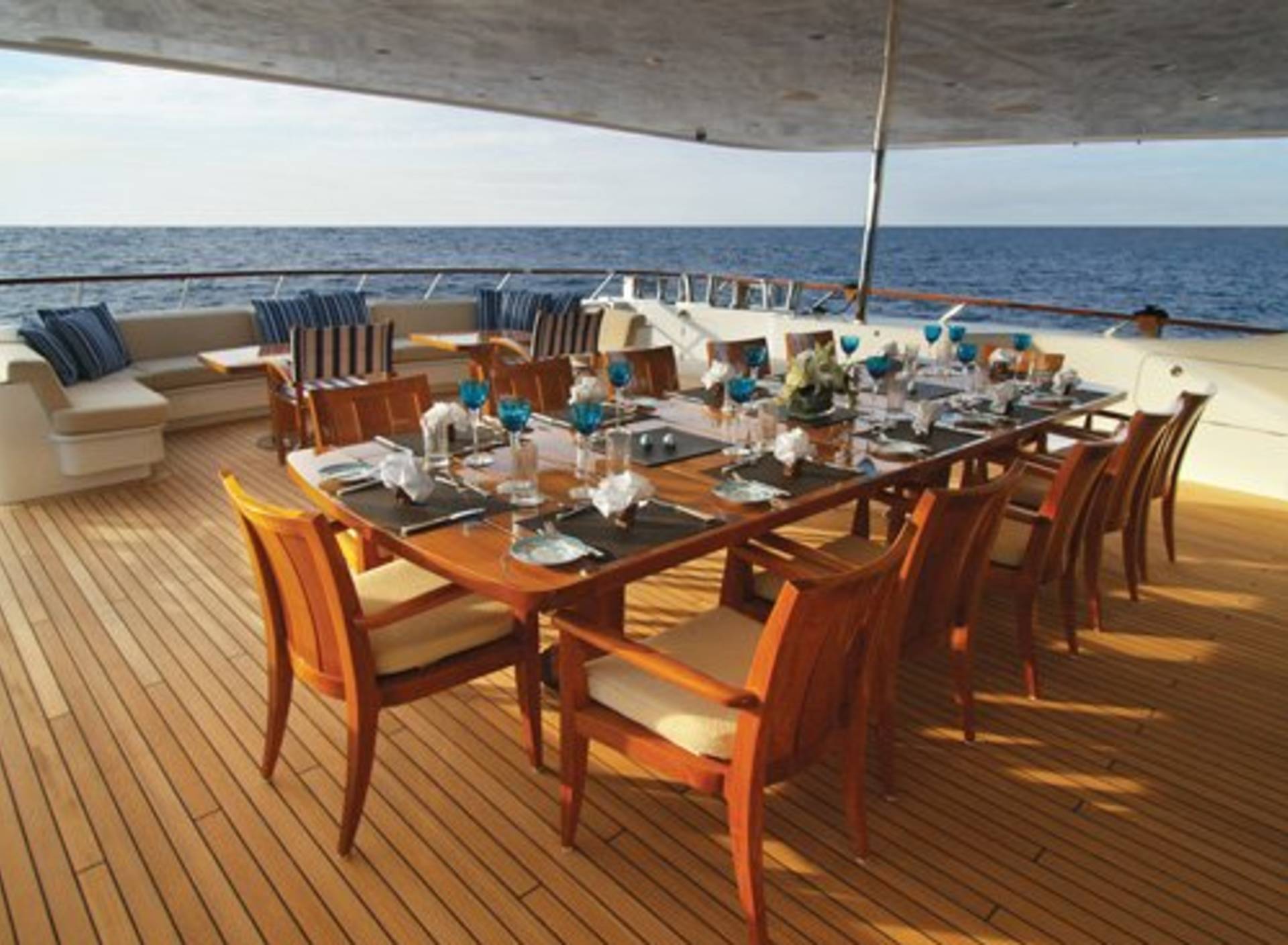 An elegant outdoor dining table is set for a feast on a luxurious yacht deck overlooking the tranquil blue sea.