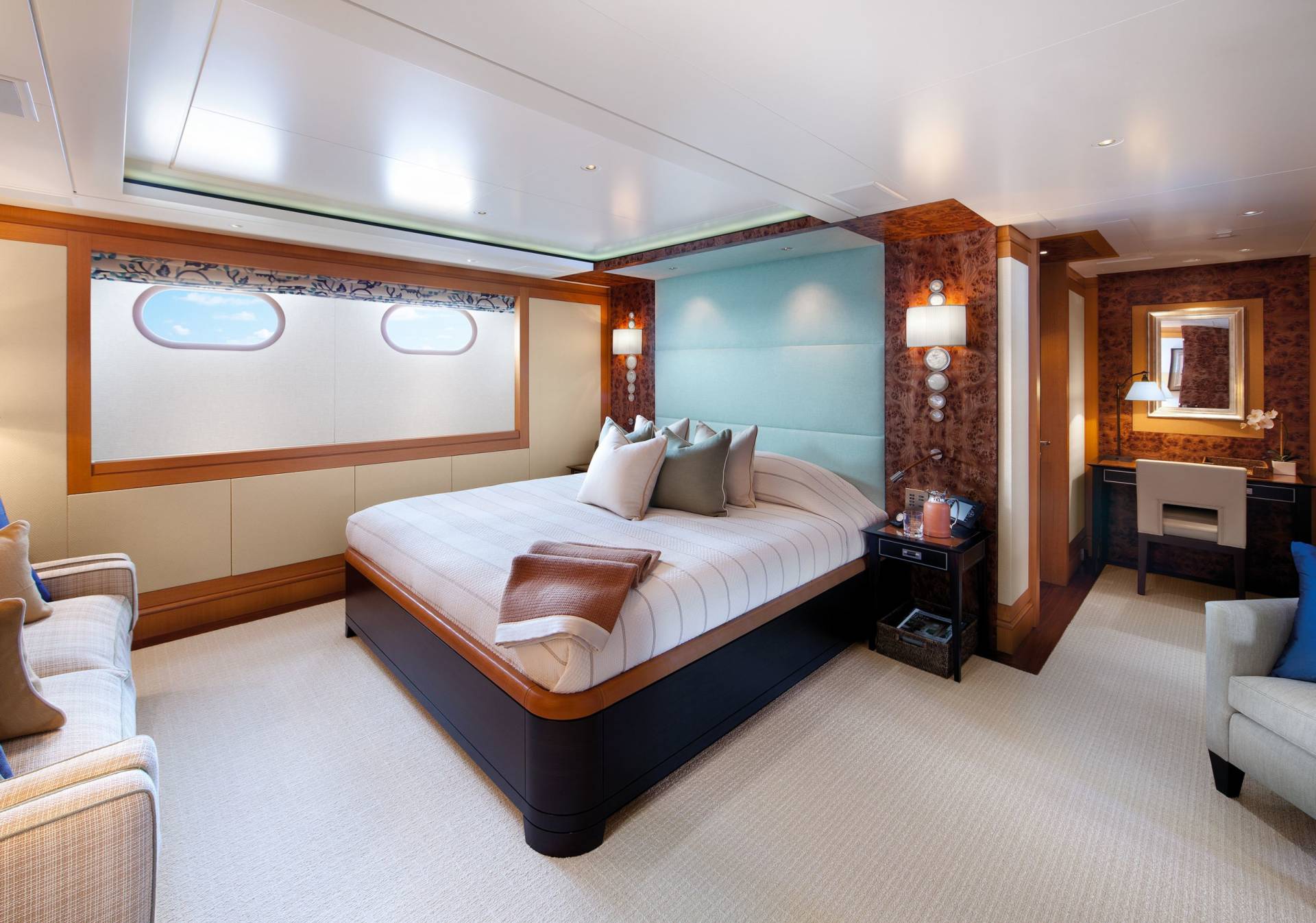 Luxurious yacht stateroom features a comfortable bed, elegant wood accents, and porthole windows offering ocean views.