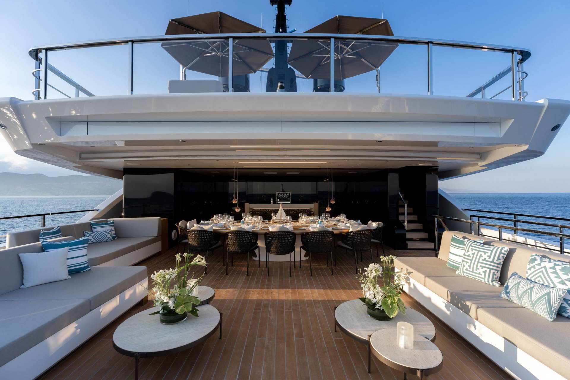 An elegant yacht deck features a formal dining table set for a feast, flanked by plush seating and overlooking the serene ocean.