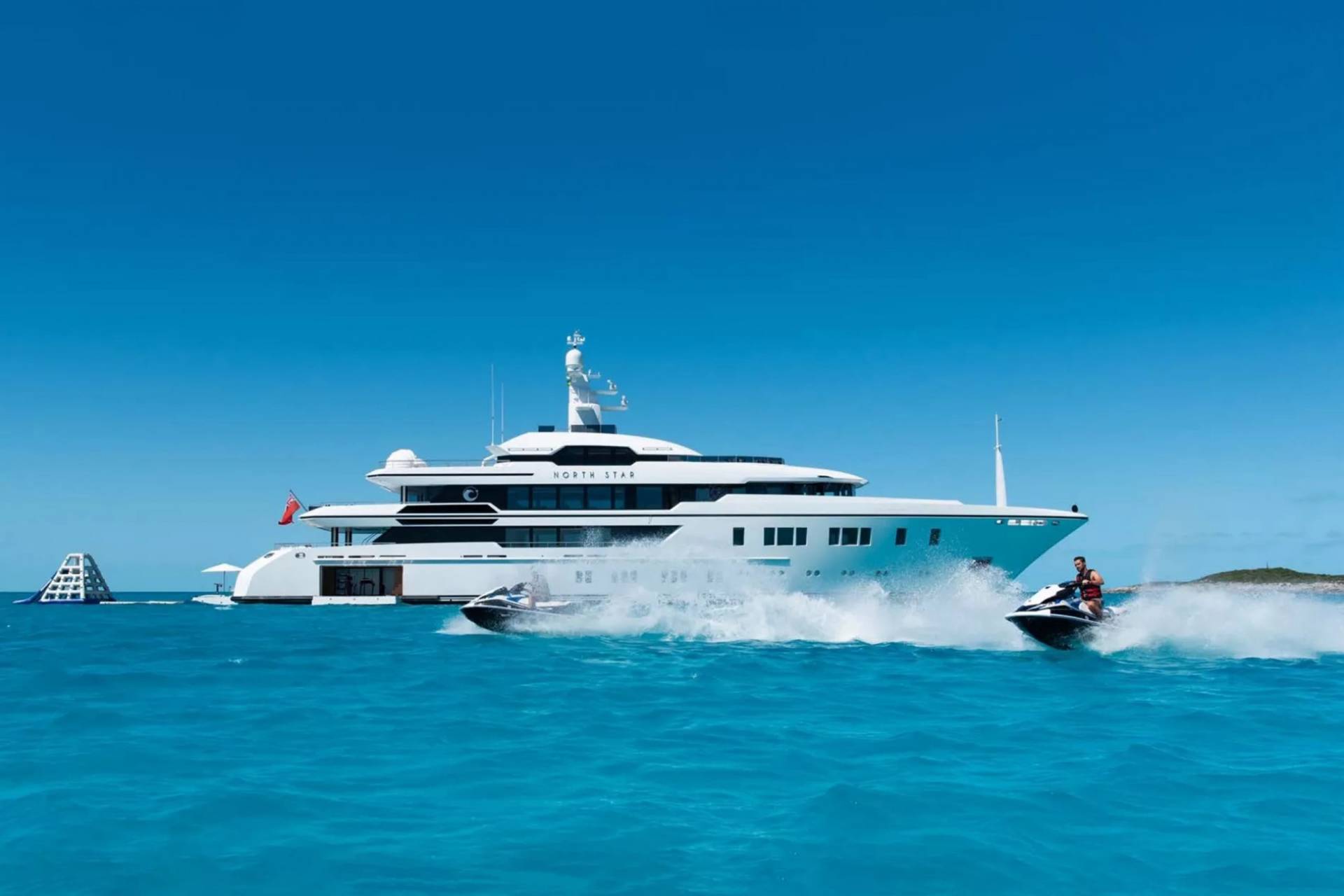 A luxurious yacht named "North Star" cruises through crystal-clear turquoise waters as jet skis race alongside.