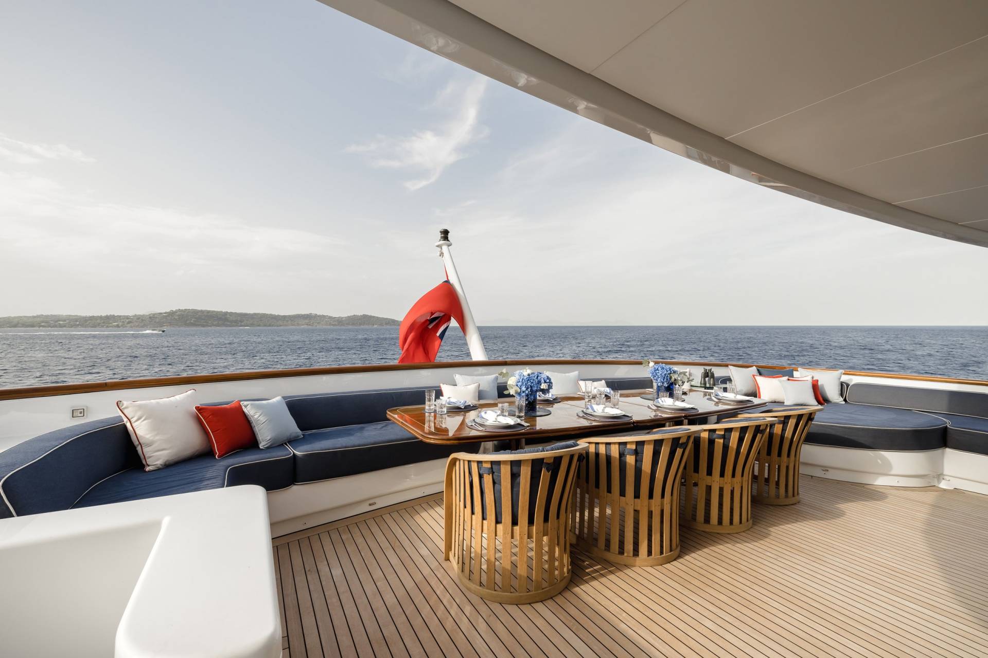 A beautifully set dining table awaits guests on the deck of a luxurious yacht, overlooking the serene blue sea.