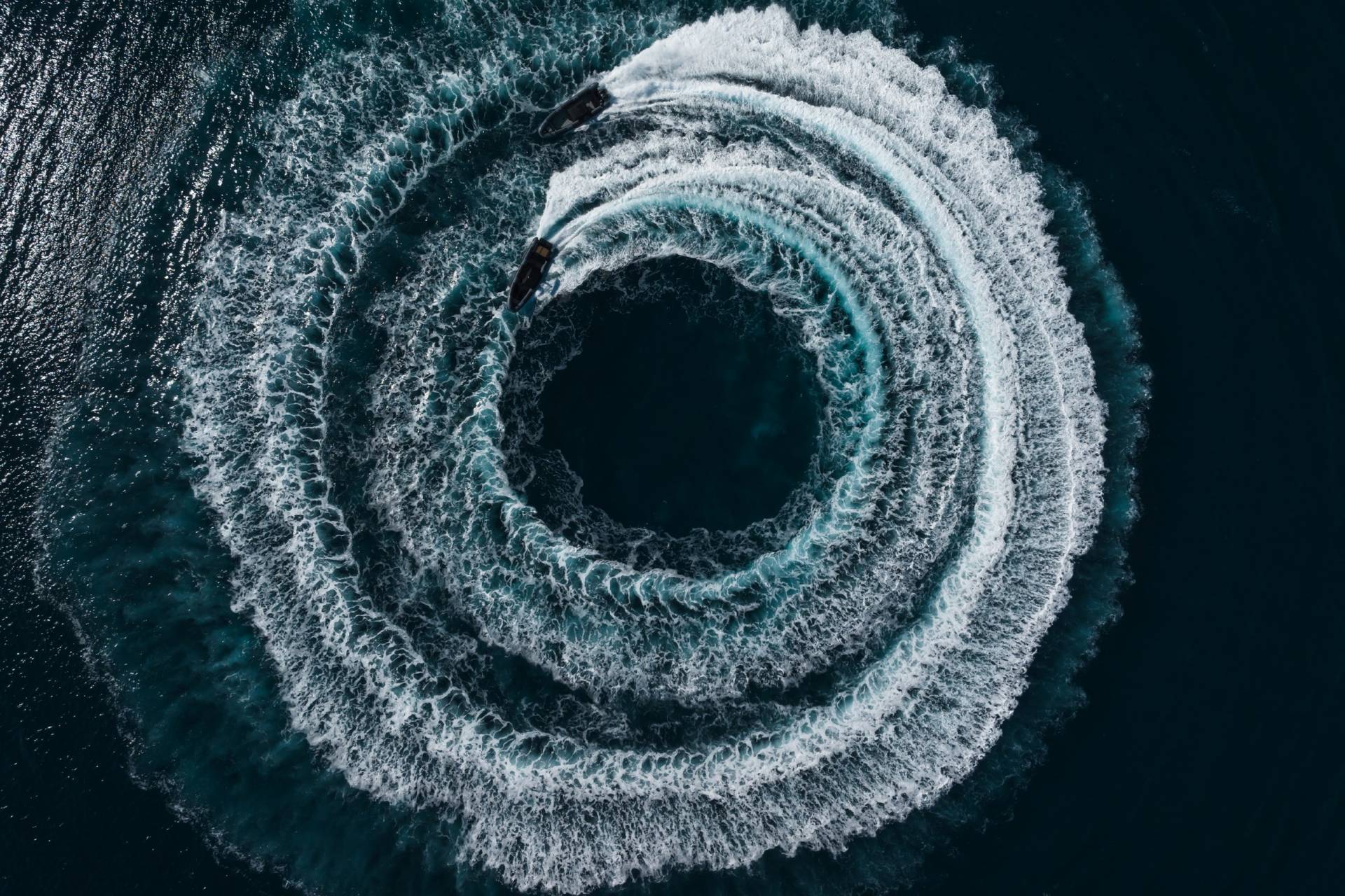 Two jet skis carve a swirling vortex of white water into the deep blue ocean.