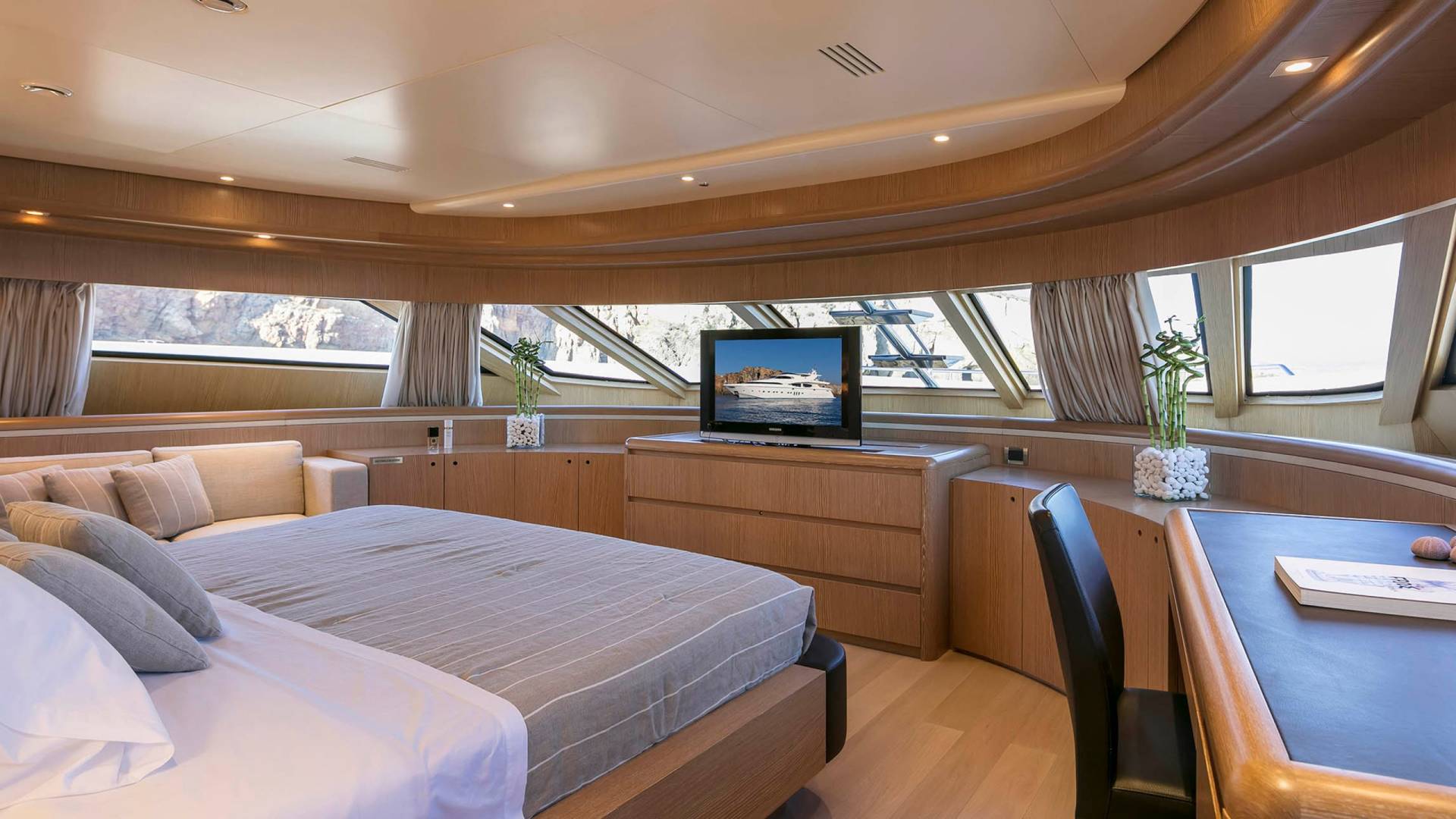 Luxurious yacht cabin features a comfortable bed, entertainment center, and panoramic windows offering stunning ocean views.