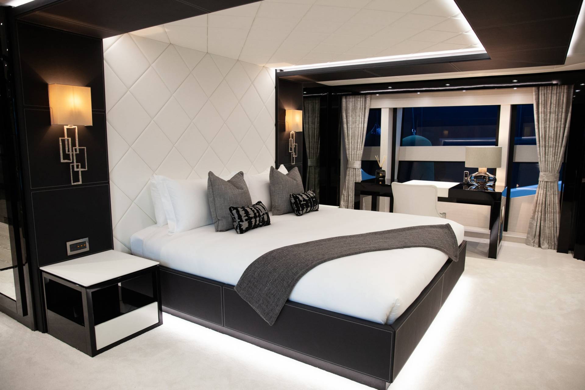 Luxurious yacht master suite features a plush bed, elegant wall sconces, and a sleek desk overlooking the water.