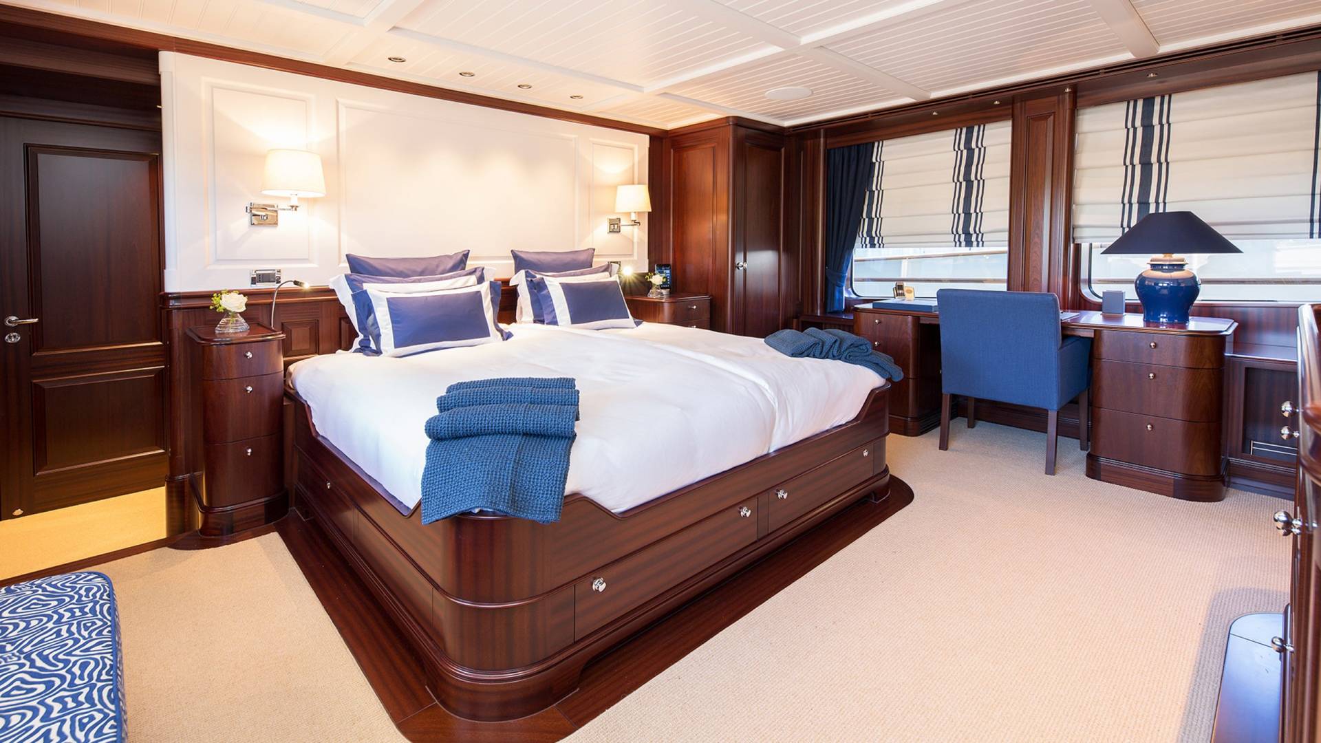 Luxurious yacht stateroom features a plush bed, elegant wood finishes, and a dedicated workspace with a view.