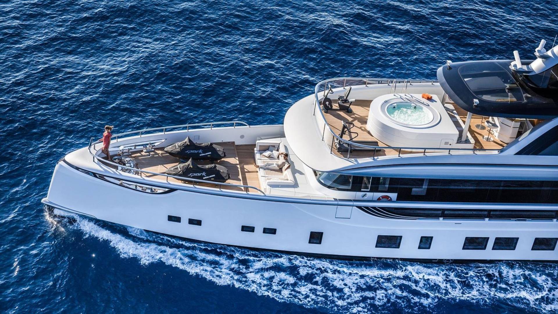 A luxurious yacht glides through the deep blue ocean, featuring a hot tub and jet skis on its deck.
