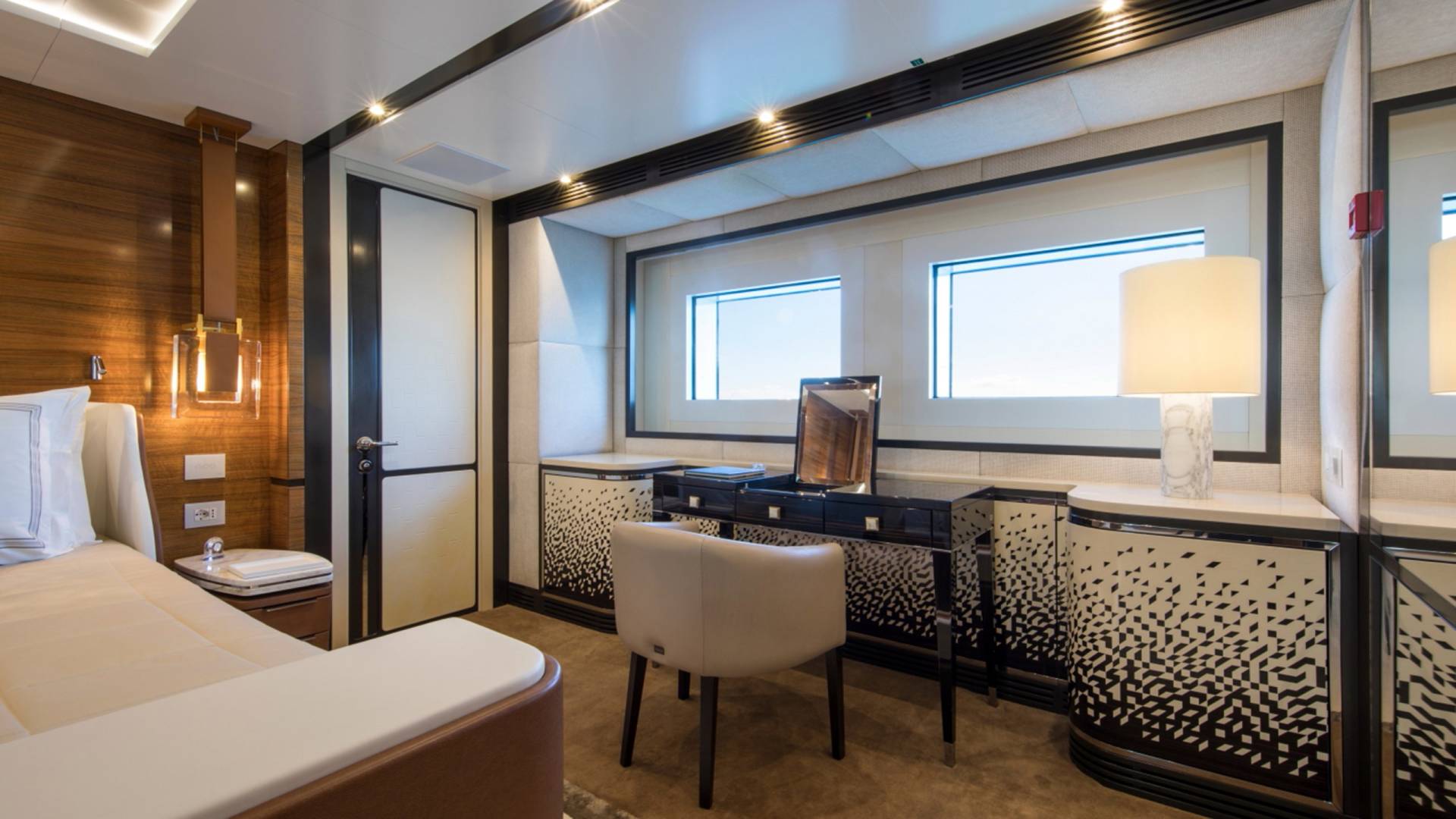 A luxurious yacht cabin features a plush bed, elegant vanity, and large windows offering ocean views.