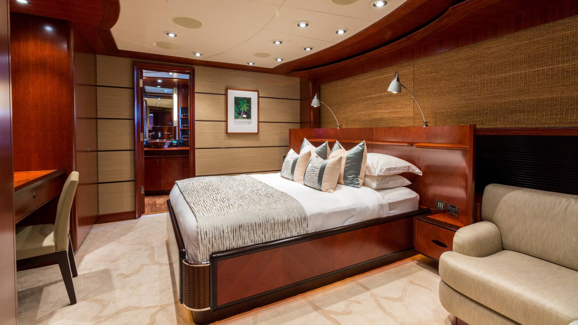 Luxurious yacht stateroom features a comfortable bed, elegant wood finishes, and a cozy armchair.