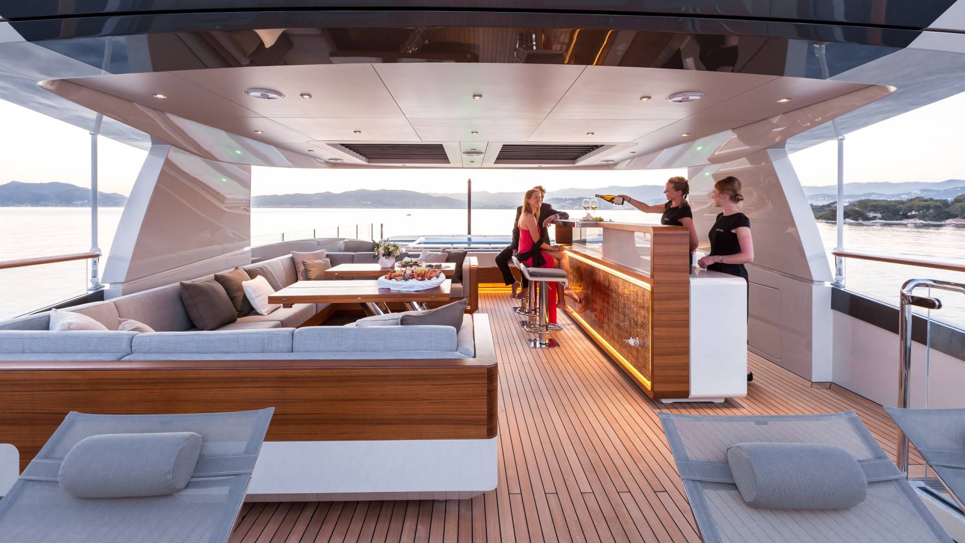 Friends enjoy drinks and appetizers on a luxurious yacht deck with a stunning ocean view.