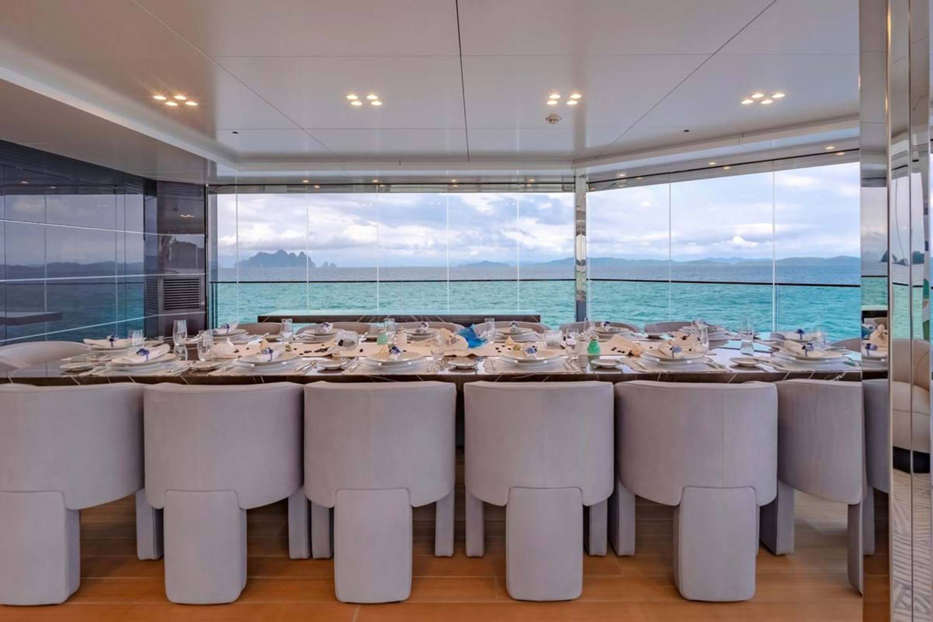 A beautifully set dining table awaits guests on a yacht, with panoramic windows offering stunning ocean views.