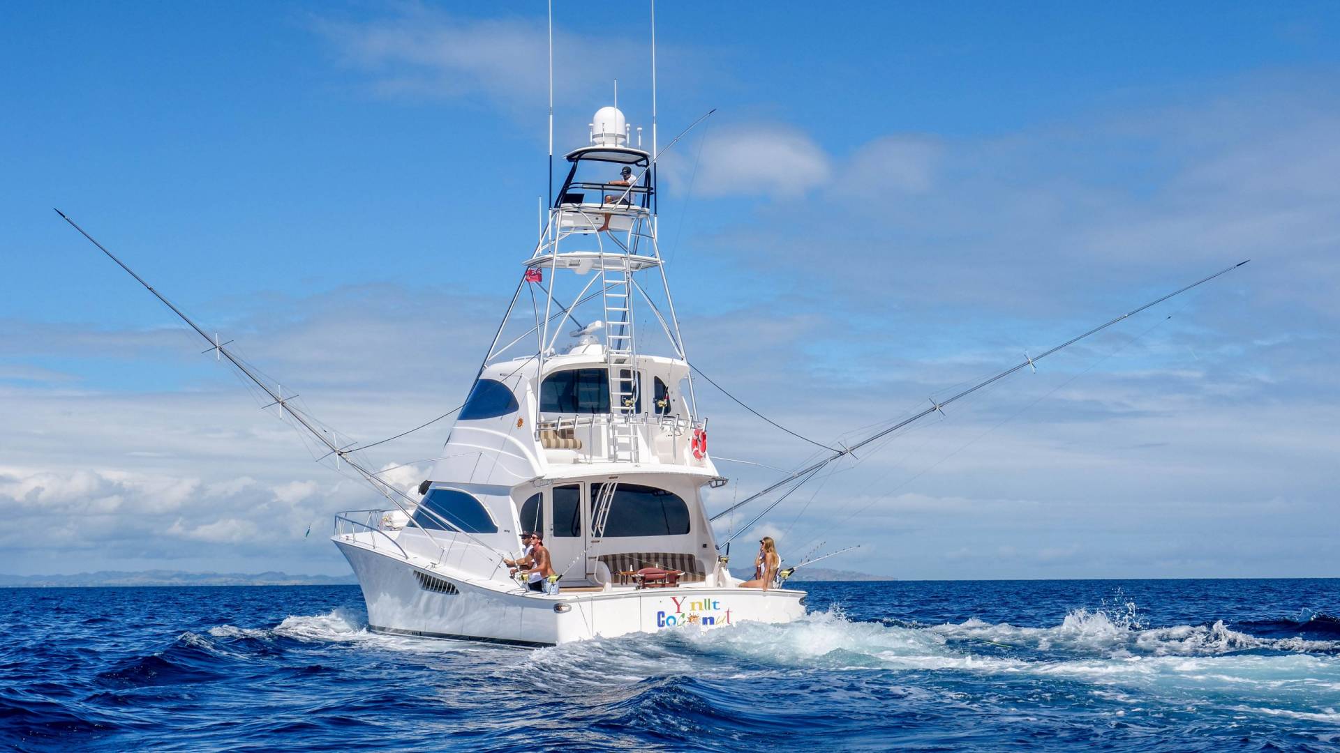 A luxurious sportfishing yacht cuts through the blue ocean waves under a bright sky.