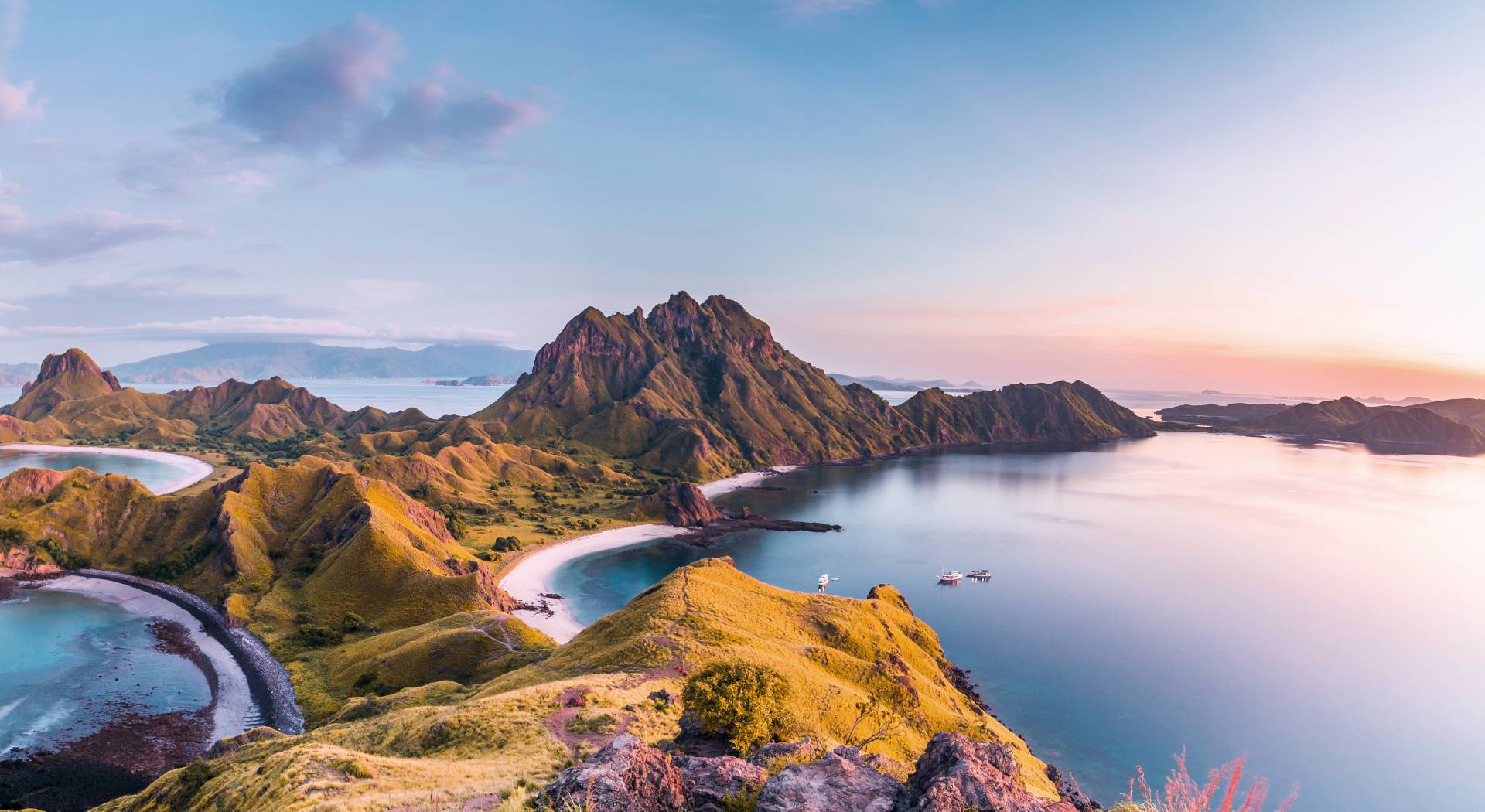 Golden hills meet turquoise waters under a pastel sky at this breathtaking Indonesian island vista.