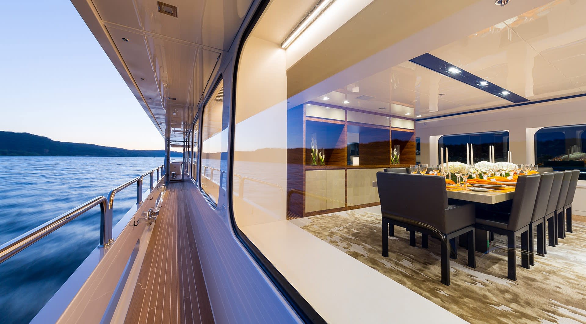 A formal dining setting awaits guests aboard a luxurious yacht cruising through serene waters at dusk.